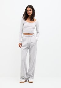 Hellgrau geschnittenes Langarm-Oberteil mit weitem Ausschnitt, kombiniert mit passenden weiten Sweatpants. Weicher Stoff, elastischer Bund und Kordelzug.