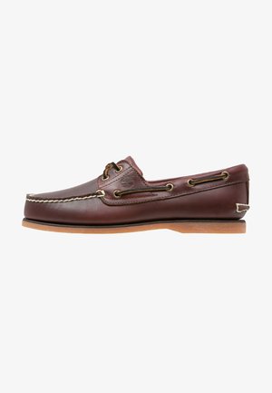 Brown leather boat shoe with white stitching, brown laces, and a tan rubber sole. Features a logo on the side and metal eyelets for laces.