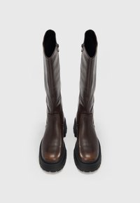 Rjavi usnjeni škornji do kolen z masivnim črnim podplatom in stranskim zadrgo, s gladko teksturo in preprosto zasnovo.