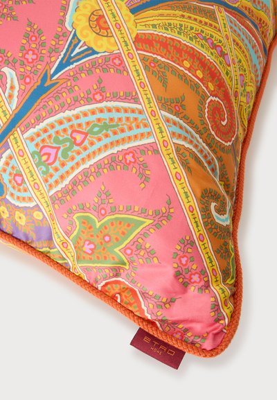Coussin décoratif avec des motifs cachemire et floraux vibrants en nuances de rose, orange, jaune, vert et violet, bordé d'un passepoil orange et d'une étiquette en tissu.