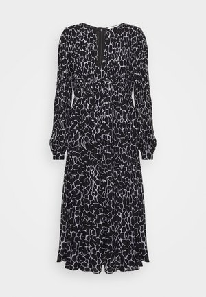 Robe midi à manches longues noir et blanc avec un motif abstrait géométrique, col rond, taille cintrée et détail de fermeture éclair au niveau de la poitrine.