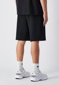 Zwarte katoenen shorts met een relaxte pasvorm, gecombineerd met witte crew sokken en grijze sneakers met zwarte accenten. Eenvoudig, minimalistisch ontwerp.