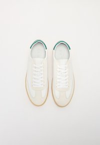 White sneakers with teal accents, featuring a smooth leather upper, round toe, and flat rubber sole. Laces are white, with a subtle texture.