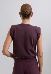 Débardeur bordeaux sans manches avec un col rond, fabriqué en tissu doux. Il présente une coupe décontractée et des coutures d'épaule visibles. Assorti à un jean taille haute.