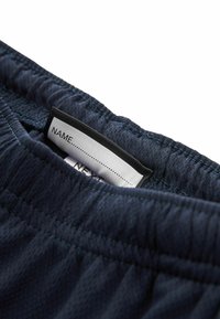Pantaloni sportivi navy con tessuto testurizzato, cintura elastica e un'etichetta che indica uno spazio per un nome all'interno.