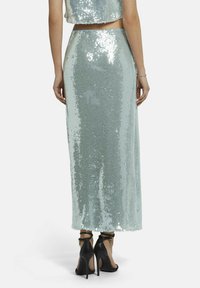 Pailletten tweedelige outfit met een cropped top en een vloerlange rok in een licht teal-kleur, met een glanzende, reflecterende textuur. Zwarte hoge hakken.