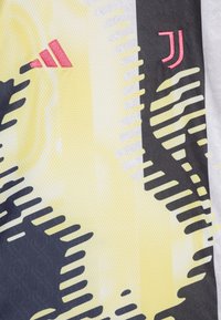 Maillot de sport Adidas en gris et jaune en matériau synthétique ; présente des motifs abstraits et des logos brodés en rouge d'Adidas et de la Juventus.