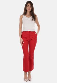 Pantaloni flare rossi su misura con una texture liscia, dotati di chiusura frontale con bottone e tasche, abbinati a un top bianco senza maniche.