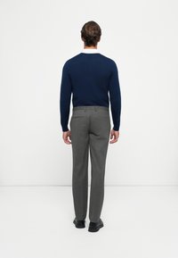 Marineblauer Strickpullover und graue maßgeschneiderte Hose. Der Pullover hat einen V-Ausschnitt; die Hose weist eine glatte Textur und Gürtelschlaufen auf. Schwarze Schuhe runden das Outfit ab.