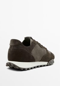 Hnědá semišová teniska s texturovaným svrškem a kontrastní šedou gumovou podrážkou. Krajkové zapínání s vyztuženou patou a texturovanou podrážkou.