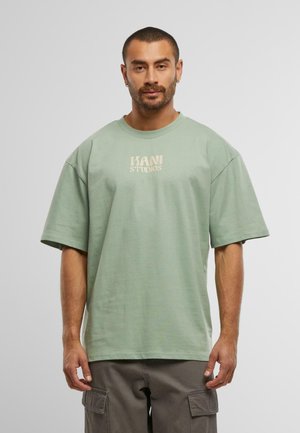 Light green oversized cotton t-shirt with dropped shoulders and a printed logo in beige on the chest. Smooth texture and relaxed fit.