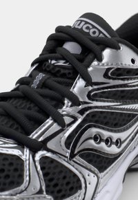 Black and silver athletic shoe with a mesh upper, textured surface, contrasting laces, and branded tongue. Features distinctive design accents.