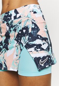 Nike sportkjol med ett flerfärgat abstrakt mönster i pastellrosa, teal och marinblått, med en inbyggd ljusblå shorts under.
