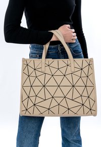 Borsa a tracolla geometrica beige con un motivo triangolare nero, dotata di manici robusti, realizzata in materiale durevole, esposta su uno sfondo bianco.
