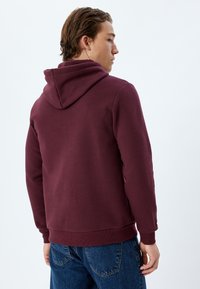 Felpa bordeaux con cappuccio e cordino, realizzata in un tessuto morbido. Presenta una tasca a marsupio e una vestibilità comoda.
