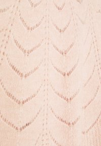 Jasnoróżowa dzianina z teksturowanym wzorem w kształcie chevronu, z delikatnymi detalami ażurowymi w całej tkaninie. Miękka i puszysta faktura.
