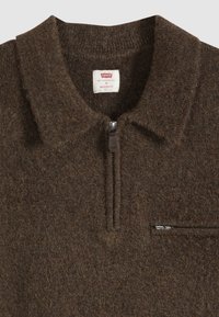 Pull en laine marron avec une demi-fermeture éclair et un col, avec une petite poche zippée sur la poitrine et une étiquette de marque Levi’s à l’intérieur du col.