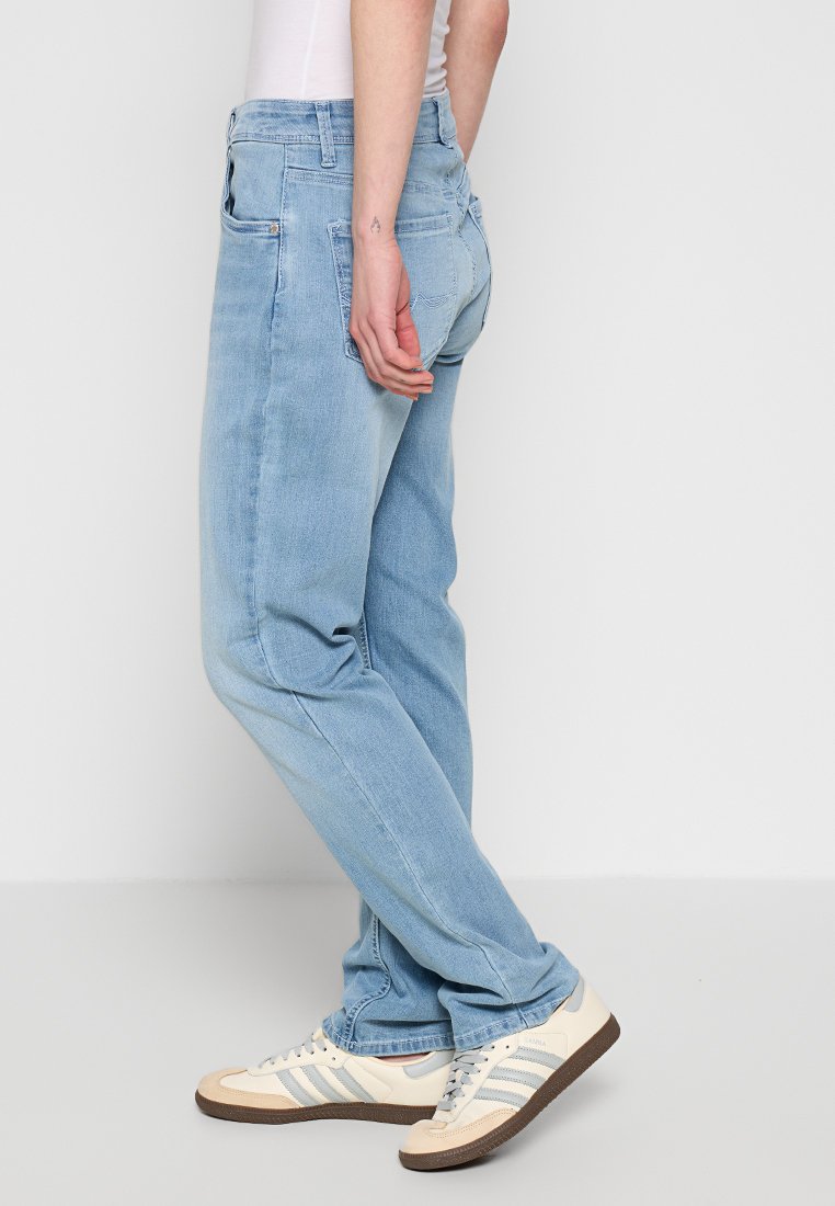 Hellblaue Jeans aus Denim, mit geradem Bein, Gesäßtaschen und einer abgenutzten Textur. Kombiniert mit cremigen Sneakers mit blauen Streifen.