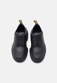 Ζευγάρι μαύρα δερμάτινα παπούτσια χωρίς κορδόνια με χοντρές σόλες και φερμουάρ στο μπροστινό μέρος, εμφανιζόμενα από πάνω σε λευκό φόντο.