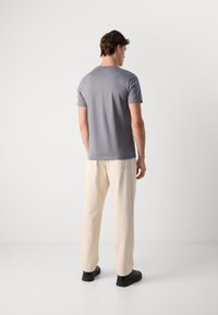 Camiseta gris de manga corta con cuello redondo, combinada con pantalones sueltos de color crema y zapatos negros, vista desde la parte trasera.