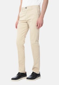 Chinos beige in cotone, con un design a gamba dritta, con zip e chiusura a bottone, abbinati a scarpe eleganti nere.