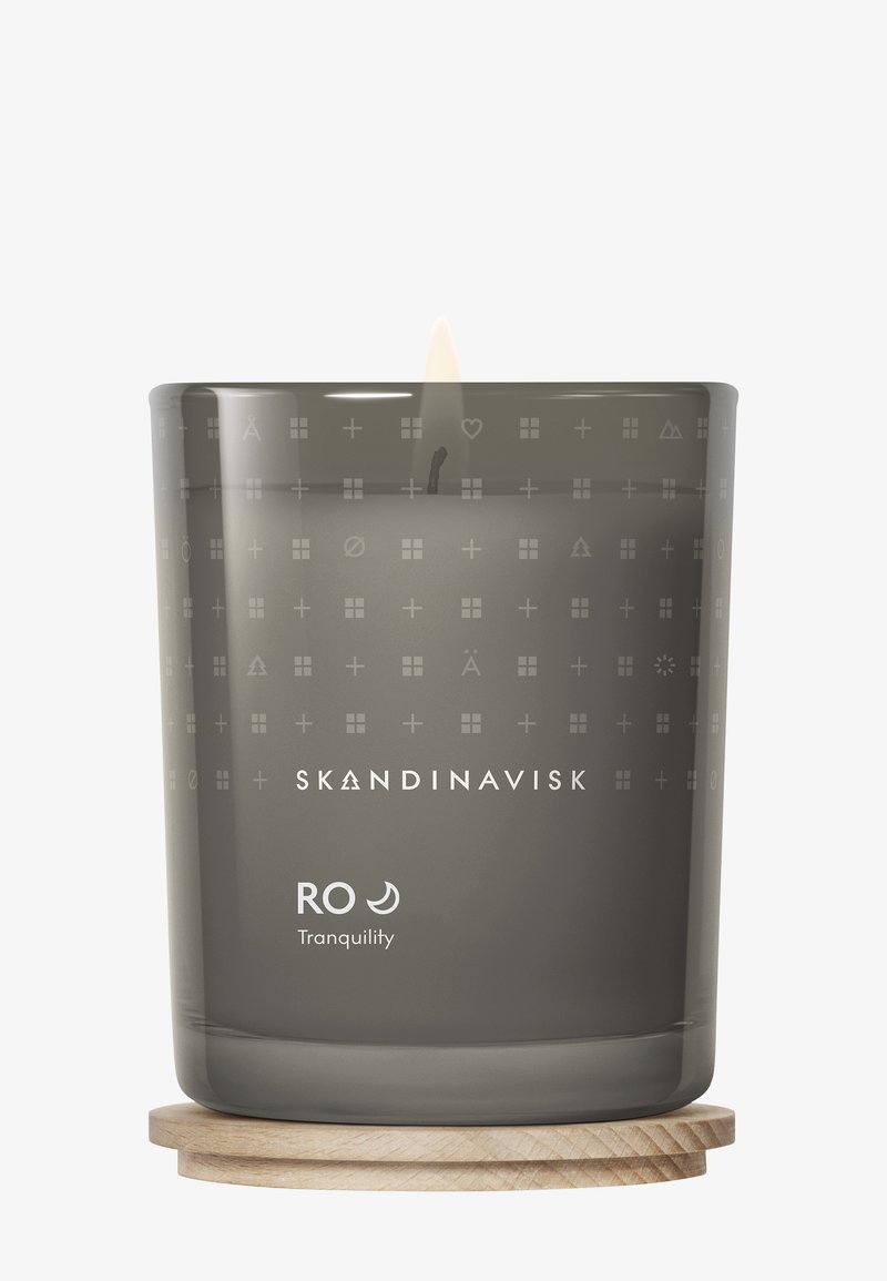 Gray glass candle with engraved patterns and text, featuring a wooden base. Lit wick visible, labeled "RO Tranquility."