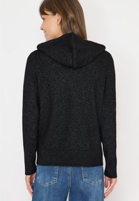 Schwarzer Kapuzenpullover mit strukturierter Oberfläche, ausgestattet mit einem gerippten Saum und Bündchen. Die Rückseite zeigt ein glattes, nahtloses Design ohne Verzierungen.