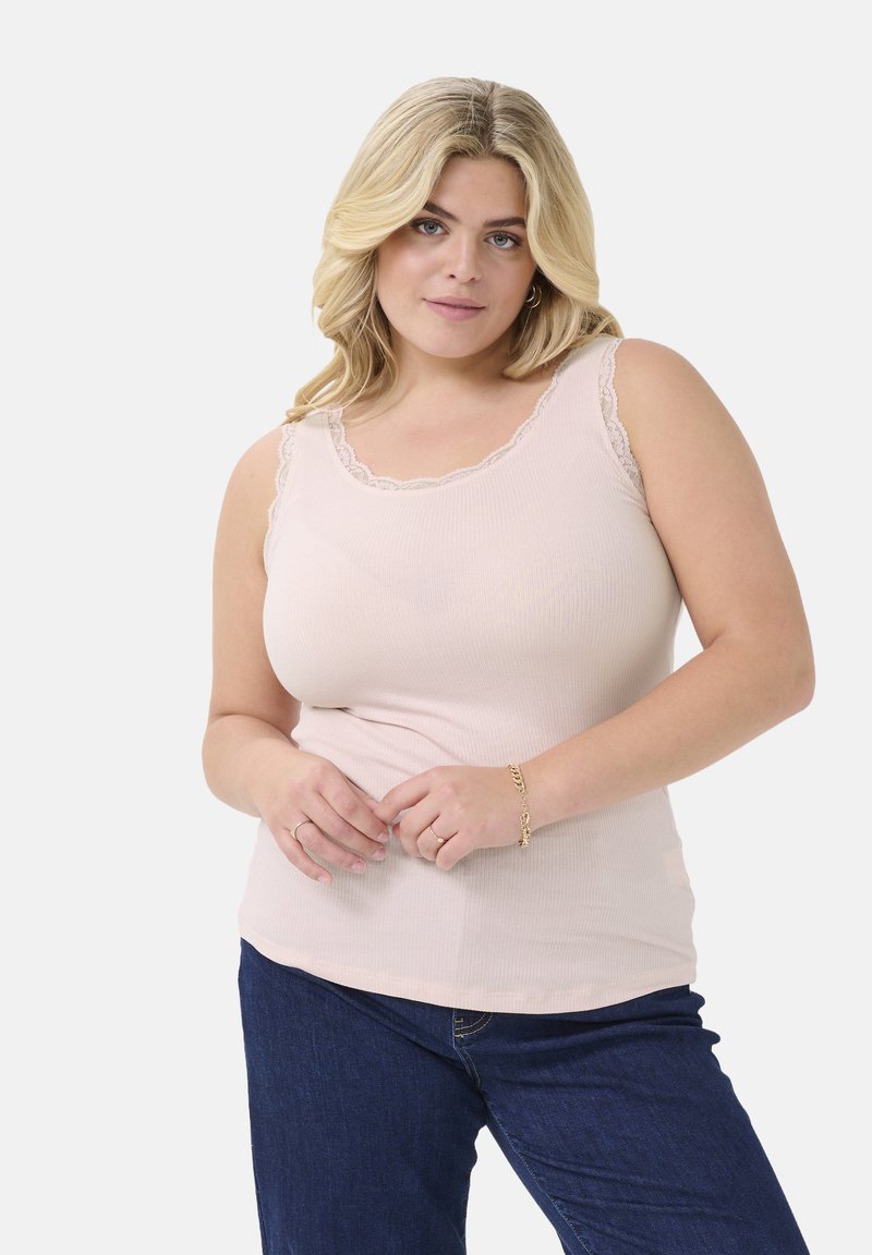 Lichtroze geribbelde tanktop met kantafwerking langs de halslijn, gecombineerd met donkerblauwe jeans. Zachte textuur, aansluitende silhoutte.
