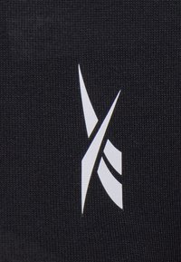 Black fabric with a textured finish features a prominent metallic white logo design made up of sharp angular shapes.