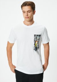 Biała bawełniana koszulka z graficznym nadrukiem postaci z "Rick and Morty" po lewej stronie, z odważnymi czarnymi i żółtymi akcentami.