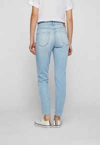 Ljusblå denimjeans med avsmalnande passform, mid-rise midja och två bakfickor. Bärs med vita sneakers med svarta och röda detaljer.