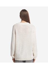 Hvid strikket sweater med løs pasform, sænkede skuldre og ribbet kant. Teksturen er blød og åndbar, ideel til lag-på-lag.