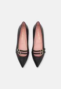 Bailarinas negras de cuero con punta afilada que presentan dos correas decorativas con hebillas doradas y una plantilla de color rosa claro. Textura suave y diseño minimalista.