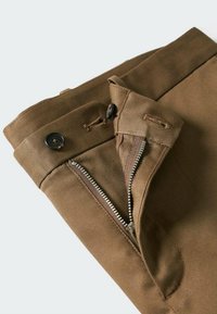 Khaki kalhoty s předním zipem, zapínáním na knoflík a plochým designem. Tkanina má hladkou strukturu a prošité detaily.