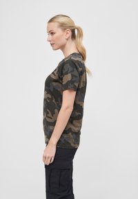 Zöld és barna árnyalatú terepmintás rövid ujjú póló, kerek nyakkivágással, puha anyagból készült, laza szabással és normál hosszúsággal.