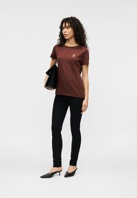 Μπορντό βαμβακερό T-shirt με κοντά μανίκια και λευκό σχέδιο στο στήθος, συνδυασμένο με μαύρο στενό παντελόνι και μαύρες μυτερές γόβες.