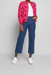 Rød bomberjakke med hvidt blomstermønster, parret med blå denim brede bukser og hvide sneakers. Enkel, afslappet outfit.