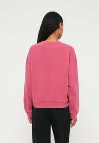 Różowa bluza z okrągłym dekoltem, opuszczonymi ramionami, ściągaczami przy rękawach i u dołu. Wykonana z miękkiego materiału o lekko teksturowanej powierzchni.