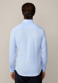 Camisa de manga larga azul claro con cuello abotonado, corte entallado y una textura suave y tejida. Cuenta con puños con botones y un dobladillo recto.
