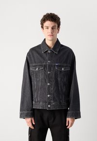 Sort denimjakke med knaplukning foran, store brystlommer og spids krave. Har en afslappet pasform og synlige syninger.