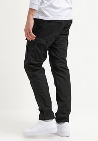 Zwarte cargobroek met meerdere zakken, taps toelopende pijpen en duurzame stof. Gecombineerd met witte sneakers voor een monochrome look.