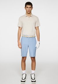 Beige pikétröja med korta ärmar, ljusblå shorts, tanbälte, vit golfhandske och svart-vita sneakers. Enkelt och sportigt design.