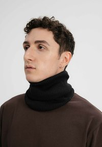 Zwarte geribbelde coltrui gedragen over een bruine top, met een dikke, gestructureerde breiwerk ontwerp. De kraag is naar beneden gevouwen, wat de volheid benadrukt.