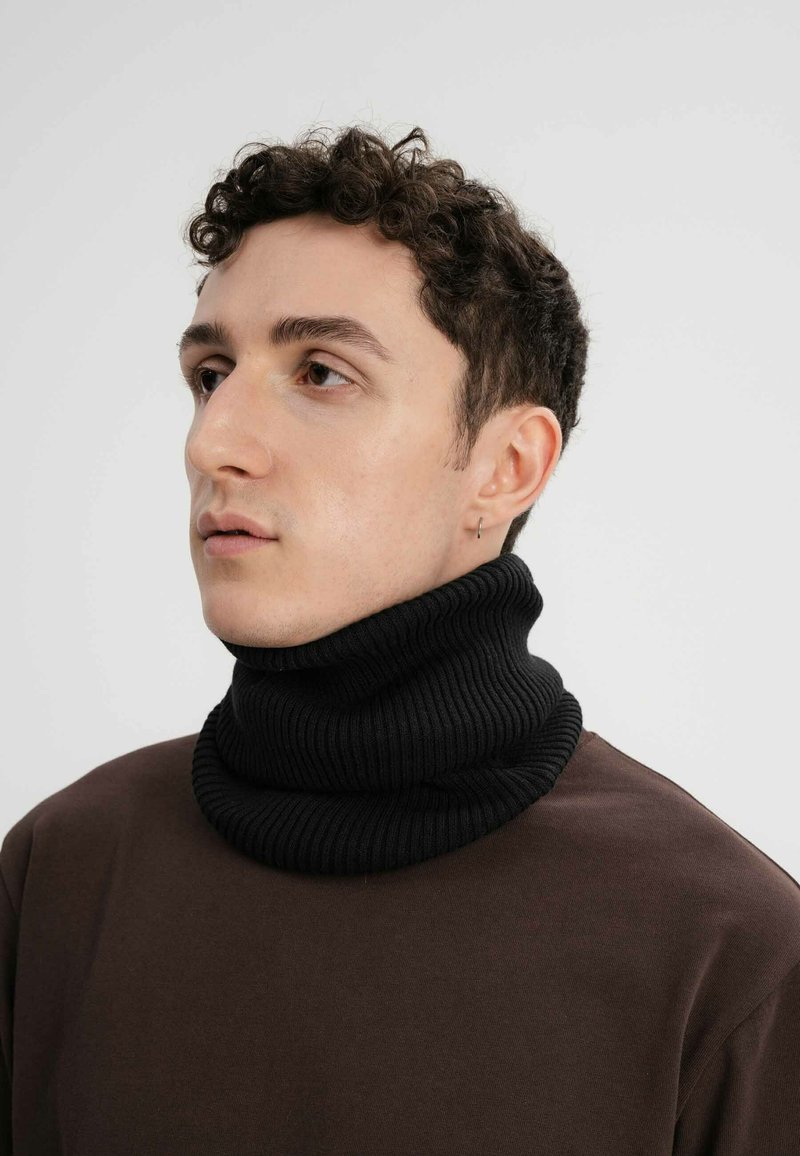 Zwarte geribbelde coltrui gedragen over een bruine top, met een dikke, gestructureerde breiwerk ontwerp. De kraag is naar beneden gevouwen, wat de volheid benadrukt.