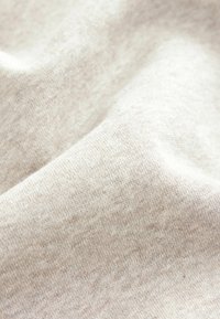 Tissu beige tricoté doux avec texture de tissage visible et plis délicats, mettant en valeur la qualité du matériau et le détail de la surface.