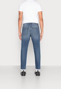 Mörkblå denimjeans med slim fit, med två bakfickor, synlig sömnad och en lätt blekt struktur. Ingen märkning synlig.