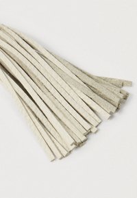 Postrzępione beżowe skórzane paski o różnych fakturach, ułożone na białej powierzchni, częściowo na siebie.