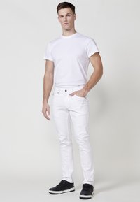 Camiseta de algodón blanca de manga corta, combinada con jeans blancos y zapatillas negras. Diseño simple, forma ajustada, detalles mínimos.
