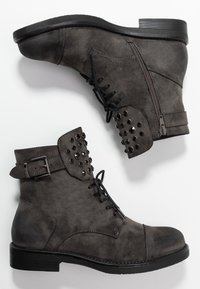 Bottines en daim gris avec un bout arrondi, fermeture à lacets à l'avant, fermeture éclair latérale et clous métalliques décoratifs sur le col et le côté. Semelle en caoutchouc noire.