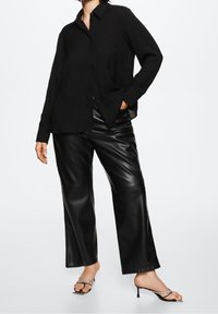 Black button-up shirt with long sleeves and a relaxed fit, paired with high-waisted black faux leather wide-leg pants and thin heeled sandals.
